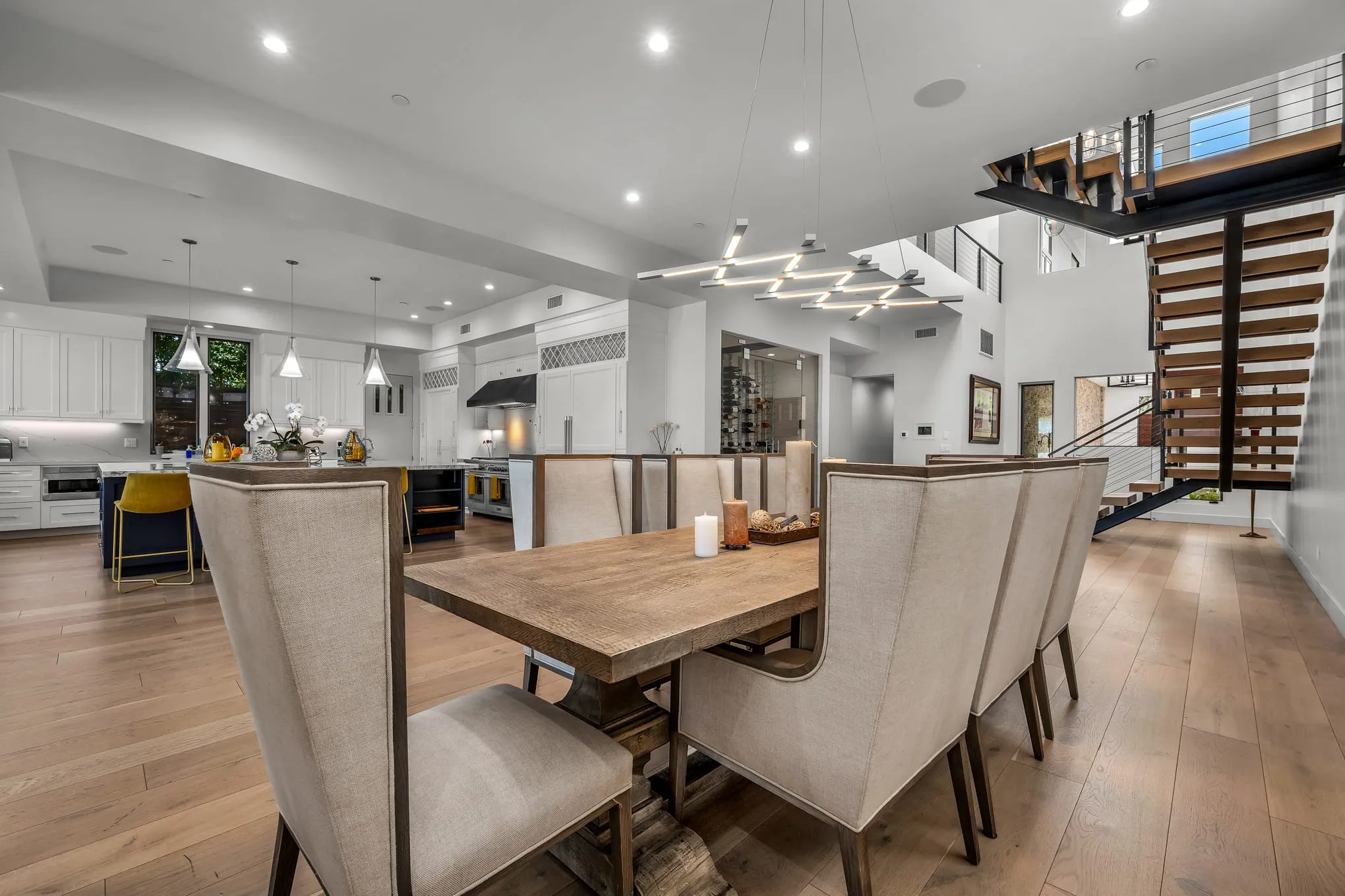 Open dining room with a long table beside the kitchen and staircase